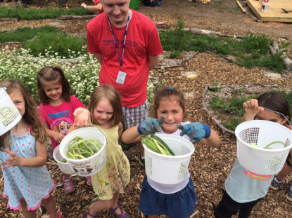 Children hold up buckets of vegetables they picked in the garden