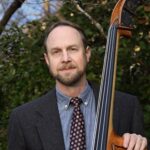 Music professor and Director of the Swannanoa Gathering, Kevin Kehrburg stands with his stand up bass and smiles.