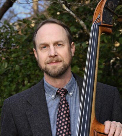 Music professor and Director of the Swannanoa Gathering, Kevin Kehrburg stands with his stand up bass and smiles.