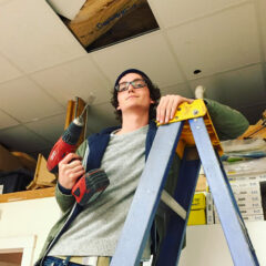 student working with drill standing on a ladder