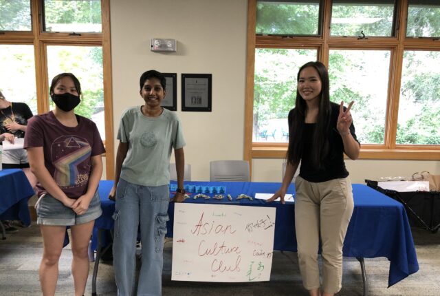 Students in the Asian Culture Club Smiling for a Picture in front of a table with a sign saying `Asian Culture Club`.