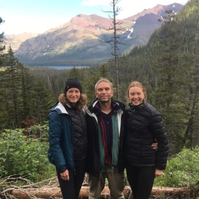 Bruce Hills stands smiling with his family with the beautiful backdrop of Glacier National Park.