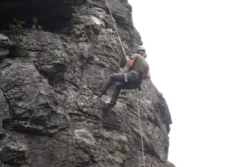 A student halfway up a cliff rock climbing.