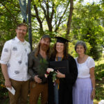 A graduate is joined by three people in a photo. They are all smiling.