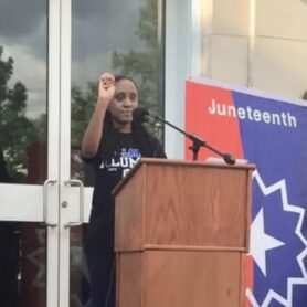 Delicia holding her fist in the air behind a podium.
