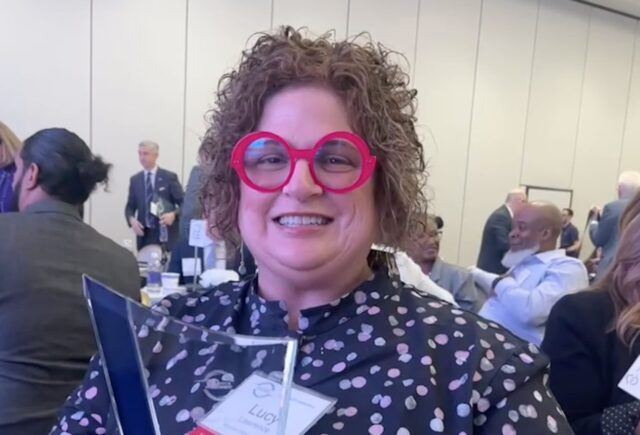 Dr. Lucy Lawrence stands at the PACE Conference holding the Engaged Faculty Award. She is wearing bright red glasses and a polka dot shirt.