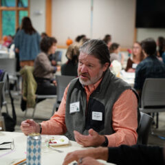 An alum sits at a table and talks to a group of students at a networking event