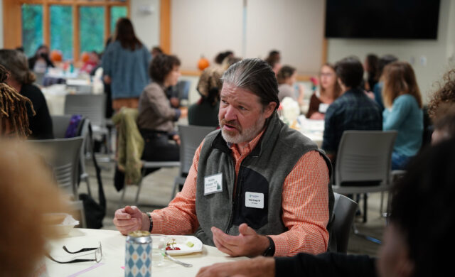 An alum sits at a table and talks to a group of students at a networking event
