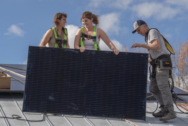 Students install a solar panel on the roof of the electric tractor barn.