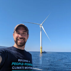 Warren Wilson Alum and Director of Chesapeake Climate Action Network Jamie DeMarco takes a selfie in front of a wind turbine on the ocean.