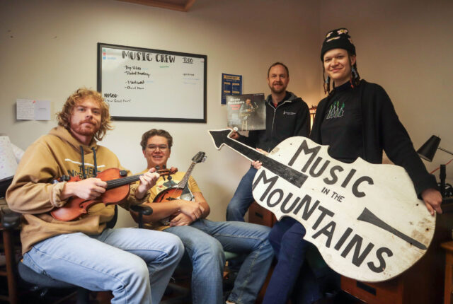3 Music Crew Students and Dr. Kevin Kehrberg sit holding instruments and a wooden sign.